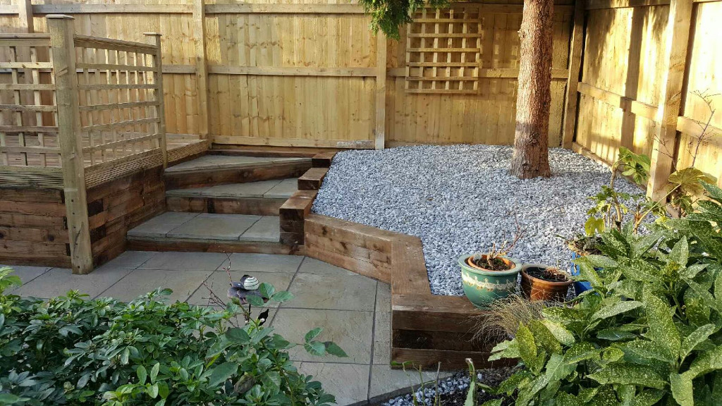 A 6ft Feather Edge fence with a patio, sleeper retaining wall, built in steps and decking, complete with trellis.